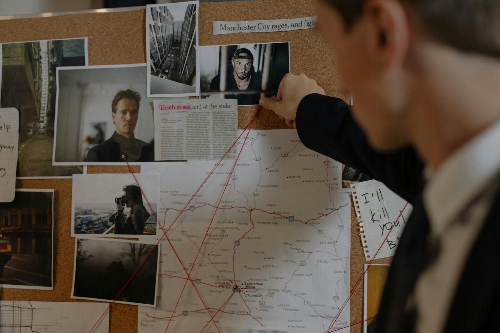 Detective examining a crime investigation board with photos, maps, and notes indoors.